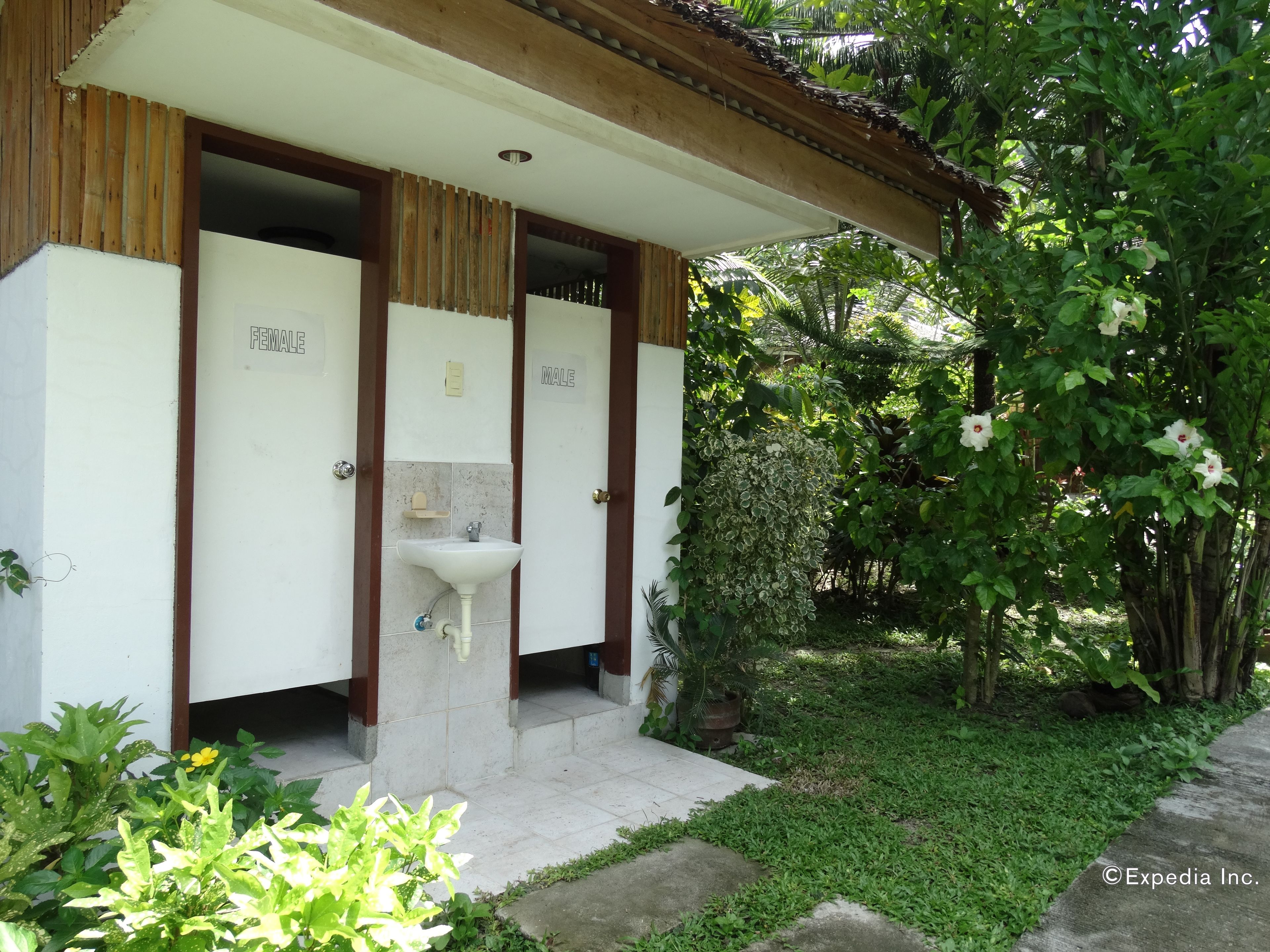 A building with separate male and female washrooms, a sink, and a garden area with various plants and flowers.