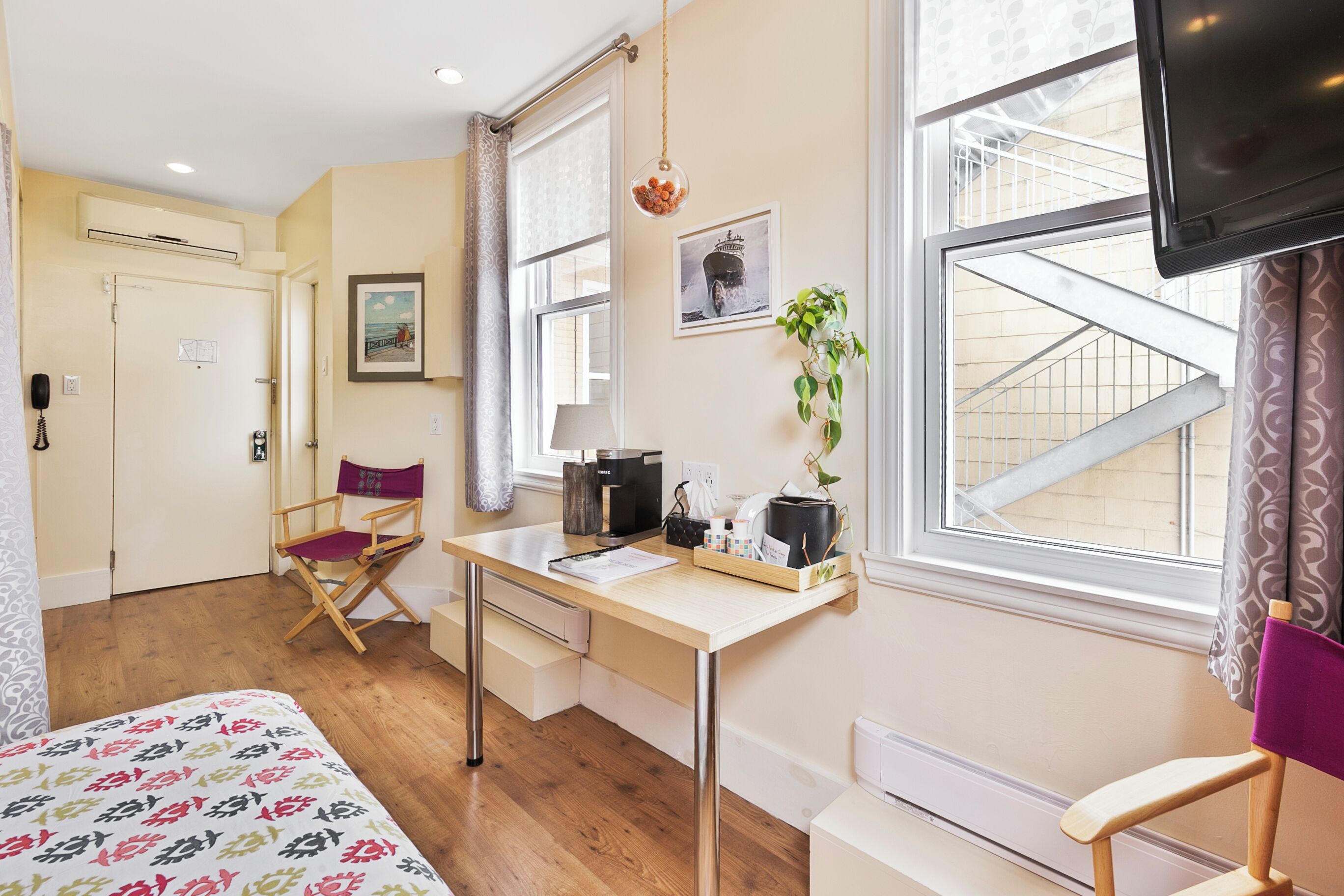A hotel room with a bed, a desk with a chair, a television, and a window with a view of a building.