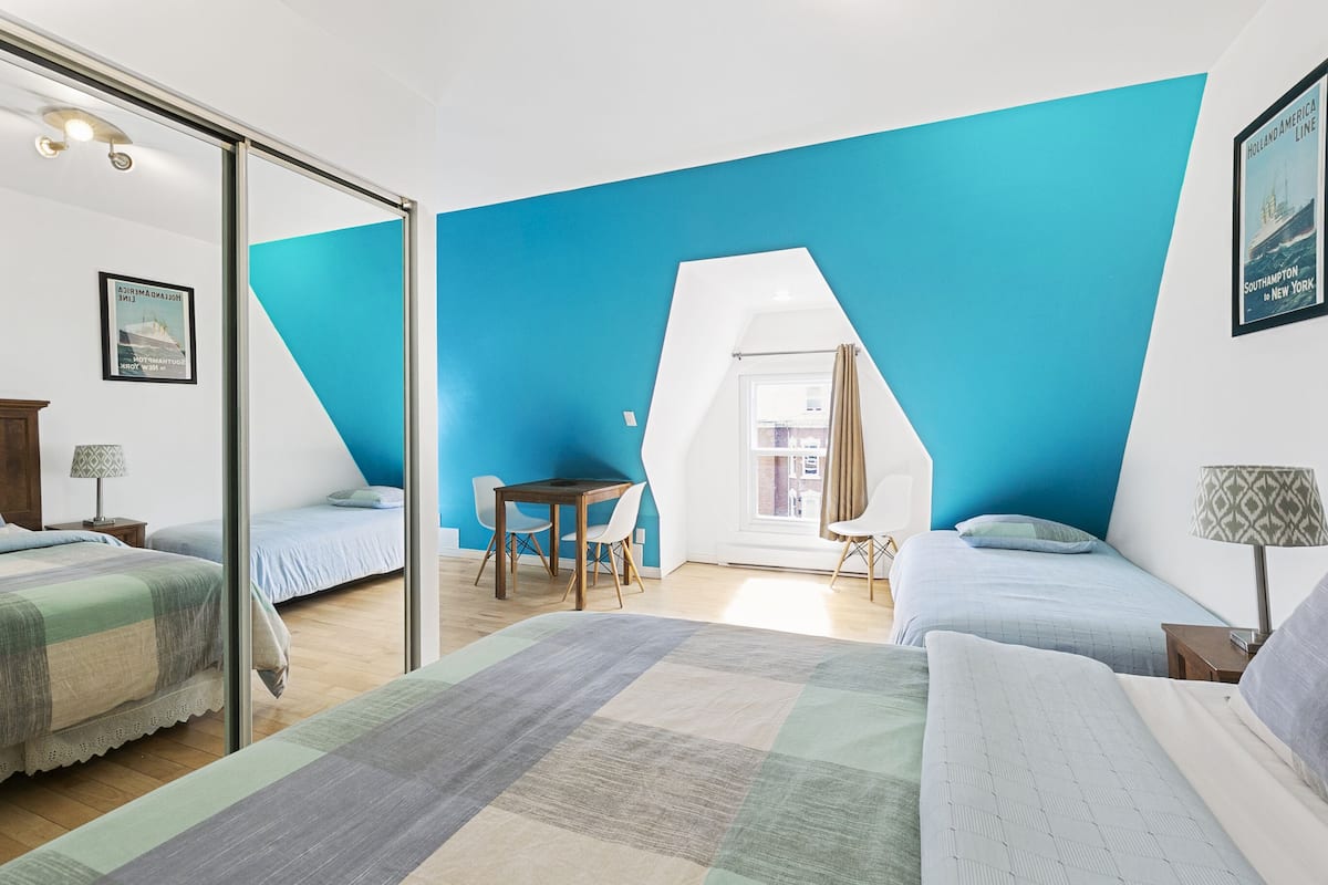 A modern bedroom with two beds, a dining table, and a large window.