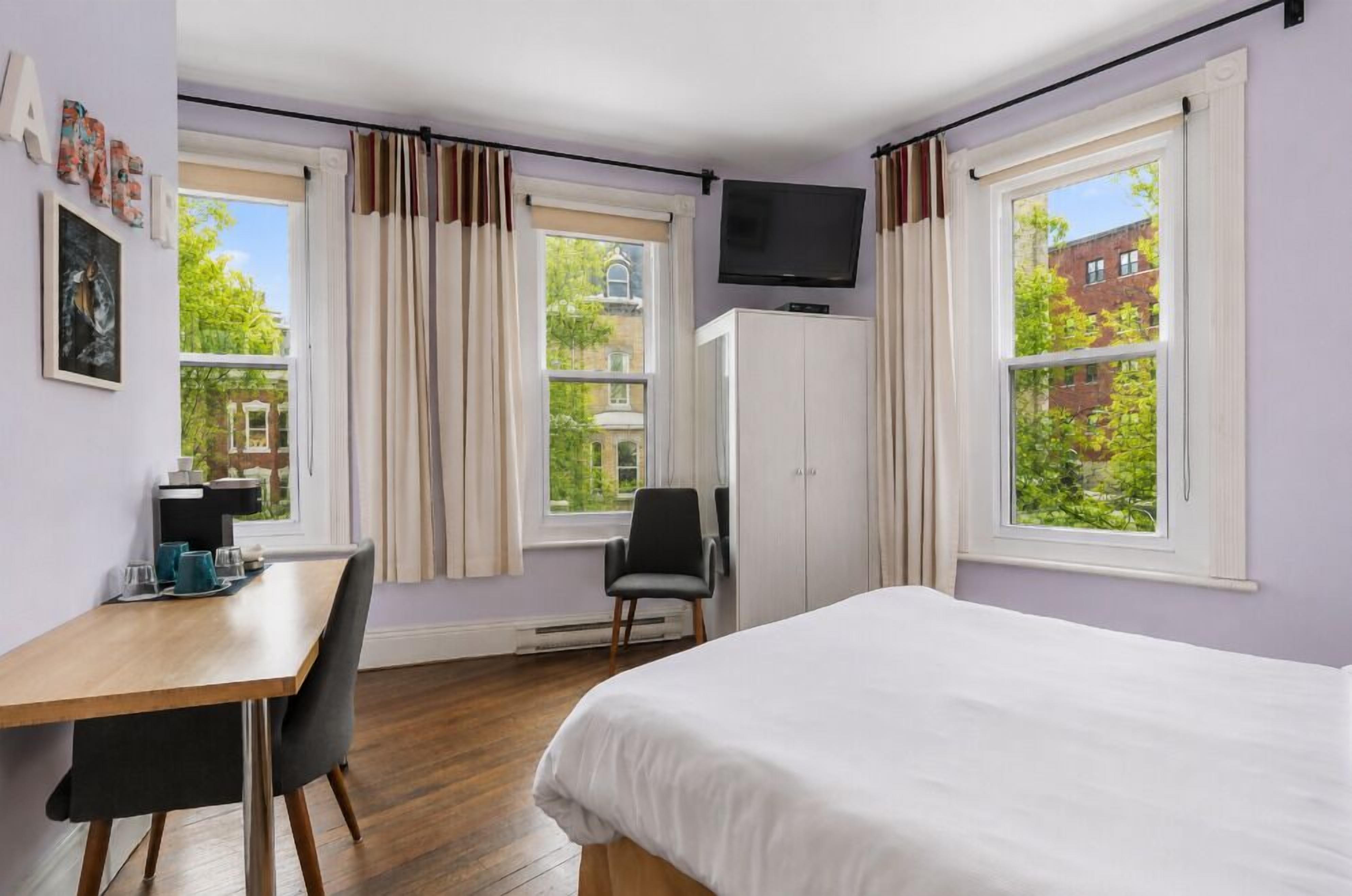 A hotel room with a bed, a desk, a chair, a television, and large windows.