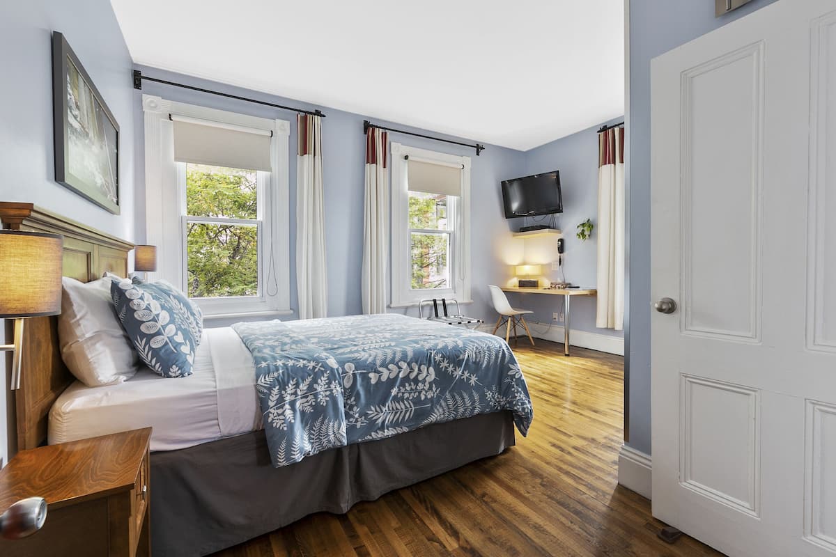 A bedroom with a bed, a desk, a chair, and a TV.