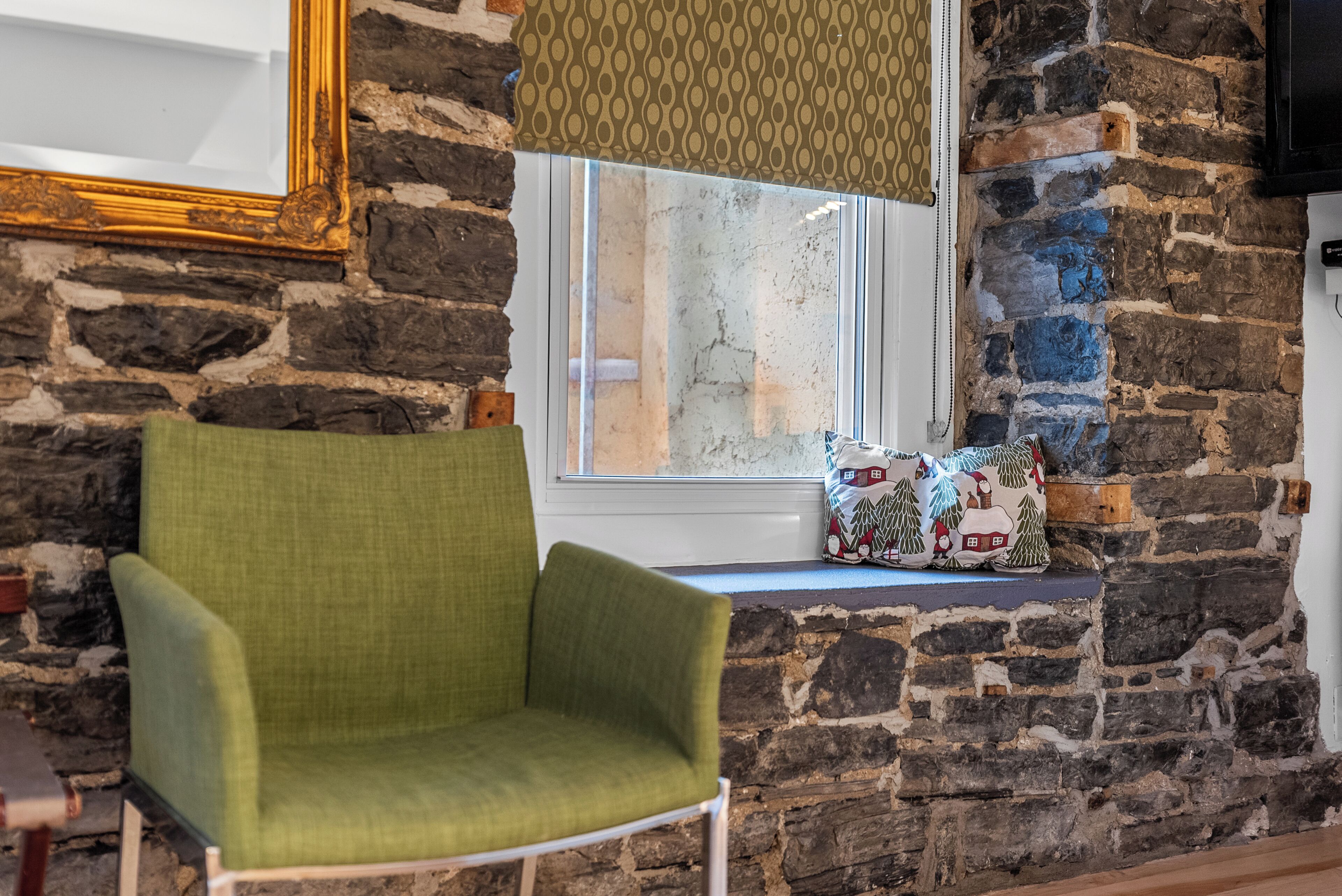A room with a stone wall, a window with a view, a green armchair, and a patterned cushion.