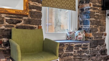 A room with a stone wall, a window with a view, a green armchair, and a patterned cushion.