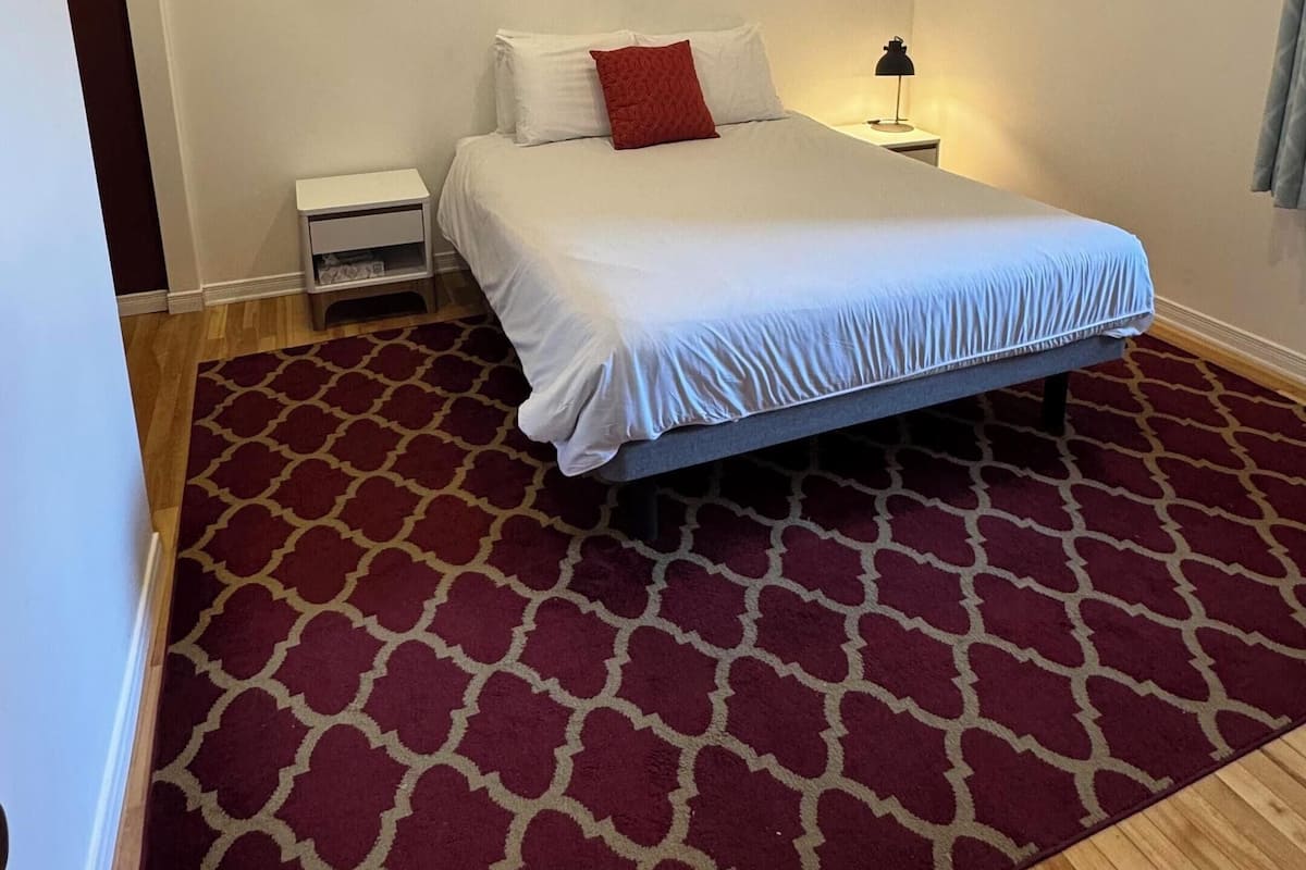 A bedroom with a bed, a nightstand, a lamp, and a patterned carpet.