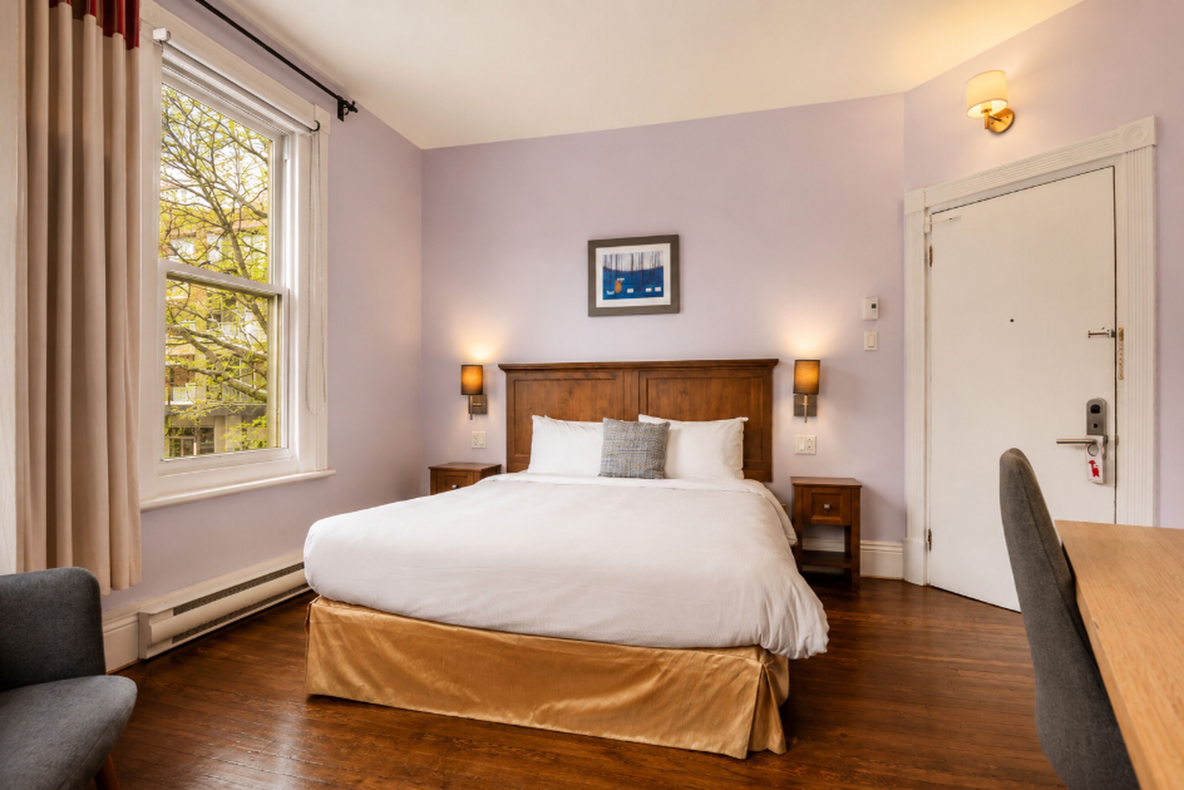 A hotel room with a large bed, a nightstand, a chair, a door, and a window with curtains.
