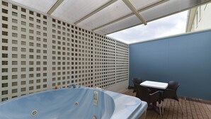 Un área de hidromasaje al aire libre con una mesa y sillas, una valla de celosía blanca y una pared azul.