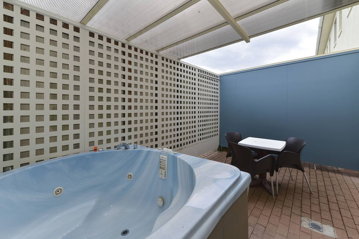 Un área de hidromasaje al aire libre con una mesa y sillas, una valla de celosía blanca y una pared azul.