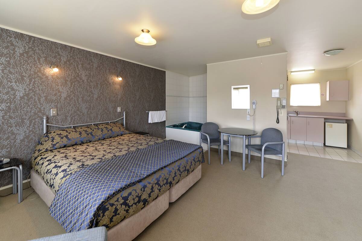 Habitación de hotel con cama, escritorio, silla y una pequeña kitchenette.