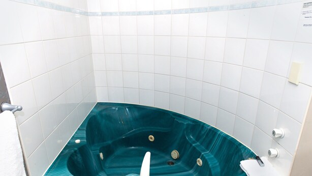 Un baño con una bañera grande de color aguamarina, paredes de azulejos blancos y una toalla blanca colgada en un perchero.