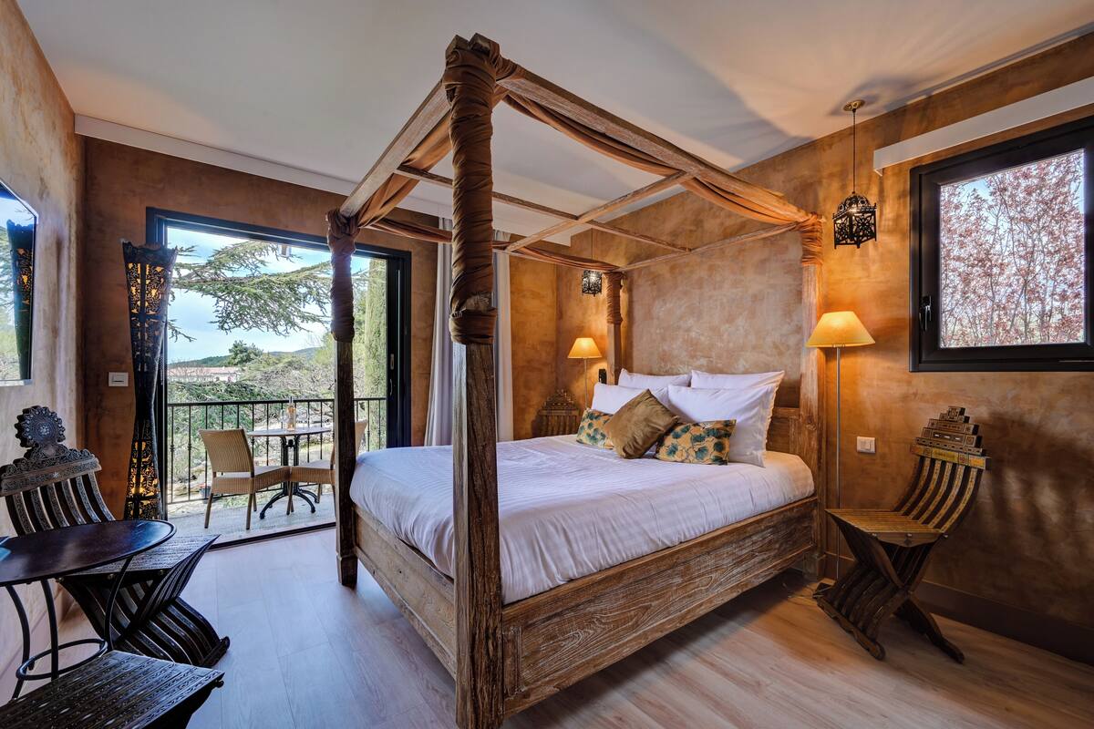 Una cama con dosel y vistas al balcón, una mesa con sillas y una silla decorativa.