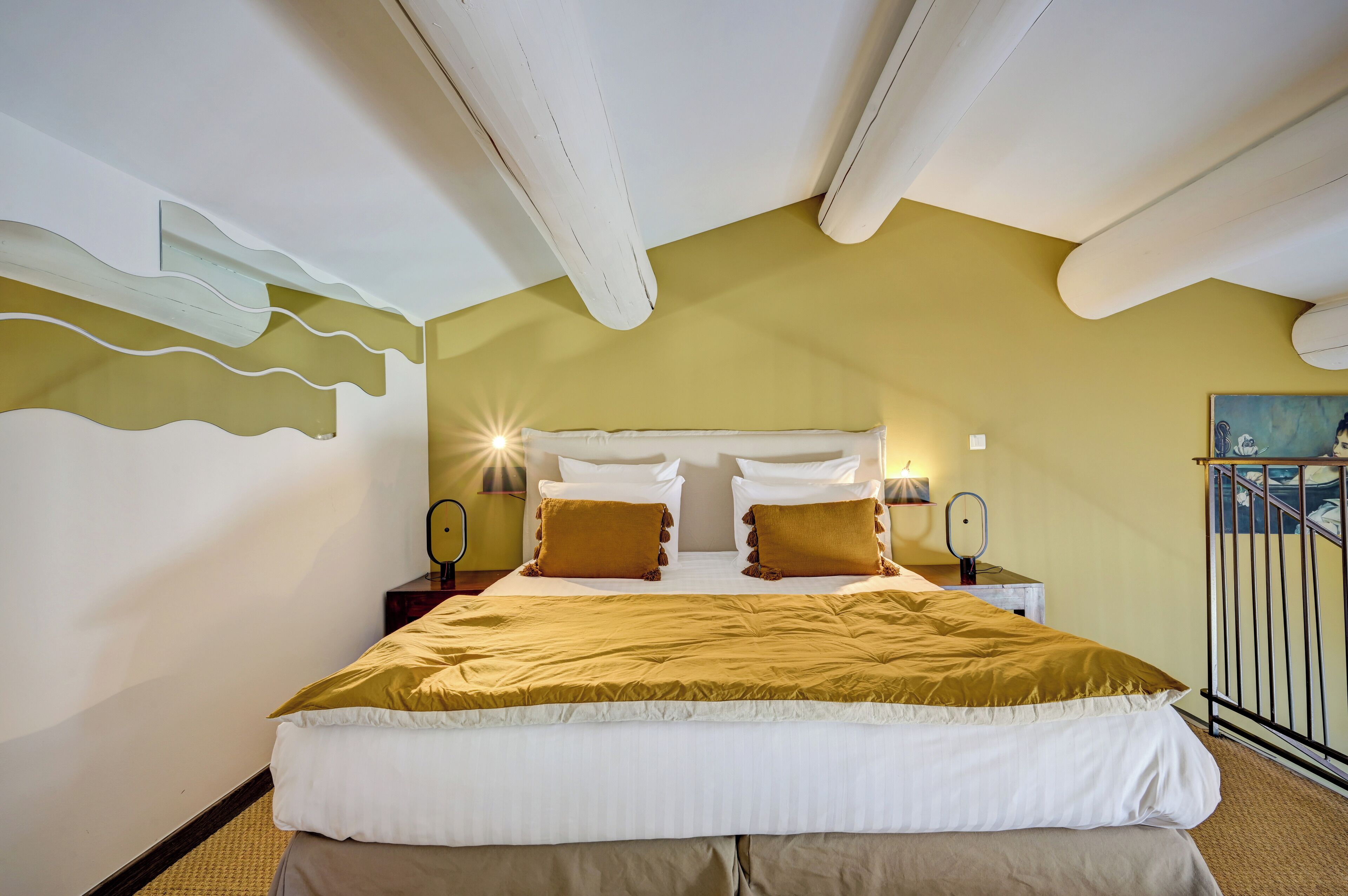 A bedroom with a large bed, two bedside tables with lamps, a headboard, and a painting on the wall.