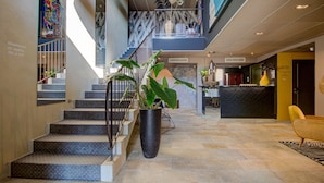 Een hotellobby met een trap, een receptiebalie en een grote kamerplant.