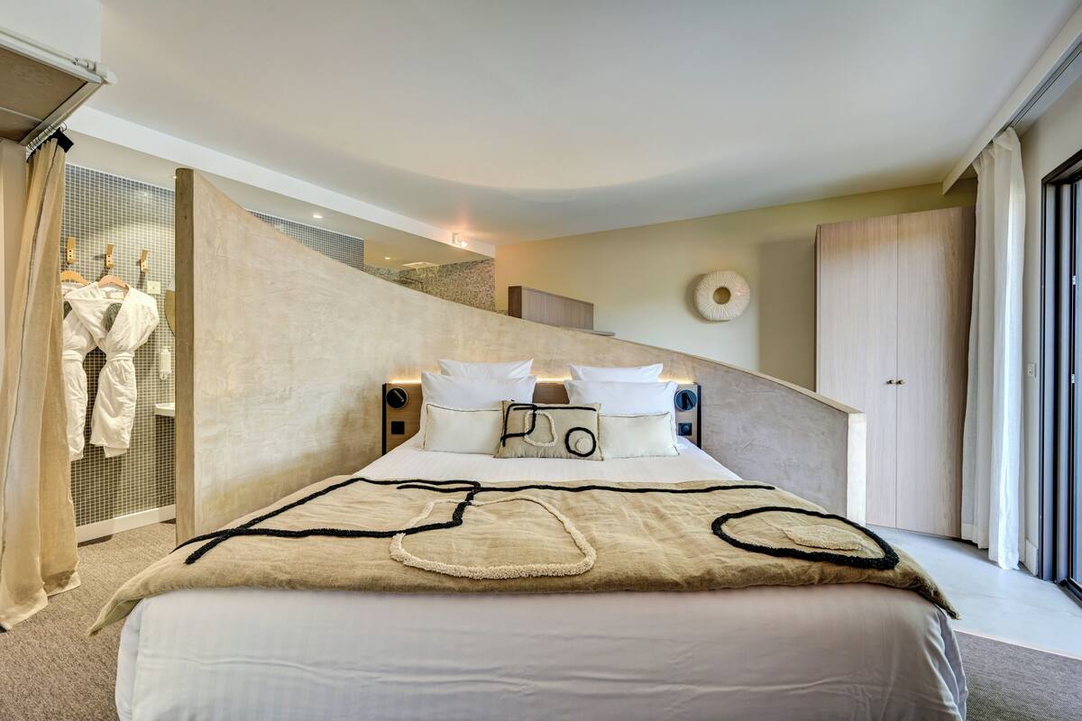 Una habitación de hotel moderna con una cama grande, un armario y un baño visible a través de una mampara de vidrio.