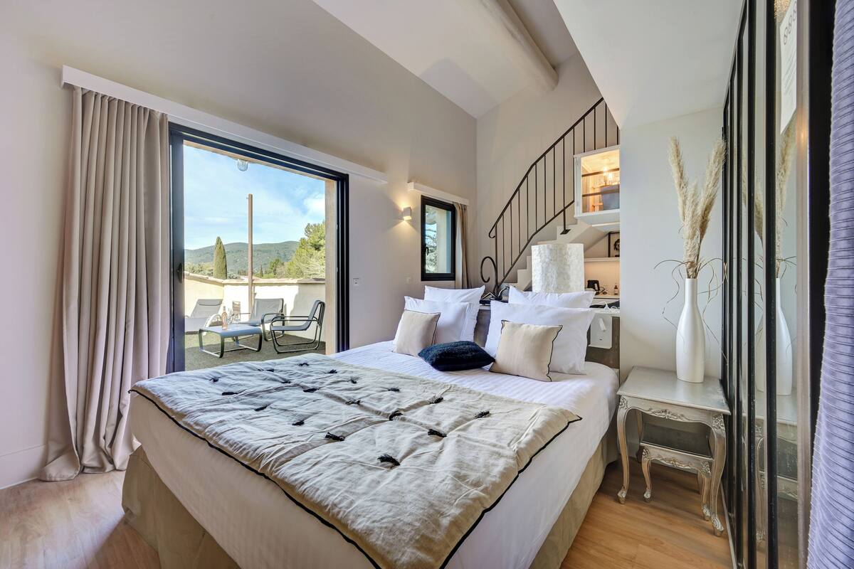 Un dormitorio con una cama grande, un balcón con sillas y vistas al exterior.