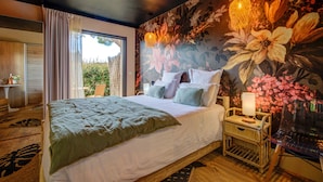 Een slaapkamer met een groot bed, een nachtkastje met een lamp, en een bloemenmural op de muur.