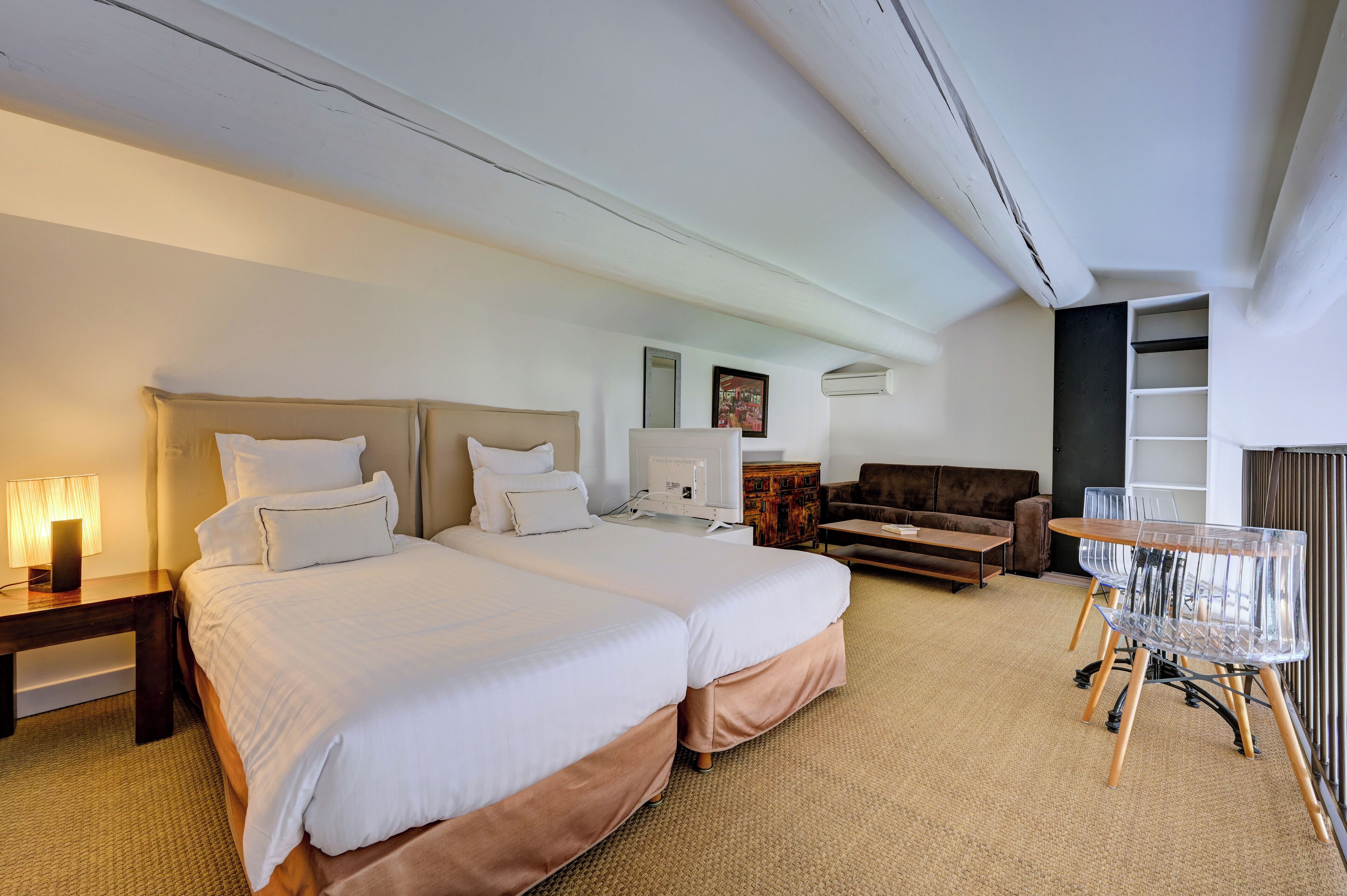 A hotel room with two beds, a sofa, a small table, and a chair.