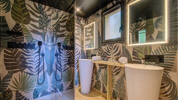 Une salle de bain avec un mur orné d’un motif de feuilles, un meuble-lavabo en bois, un grand miroir et une douche avec une porte en verre.