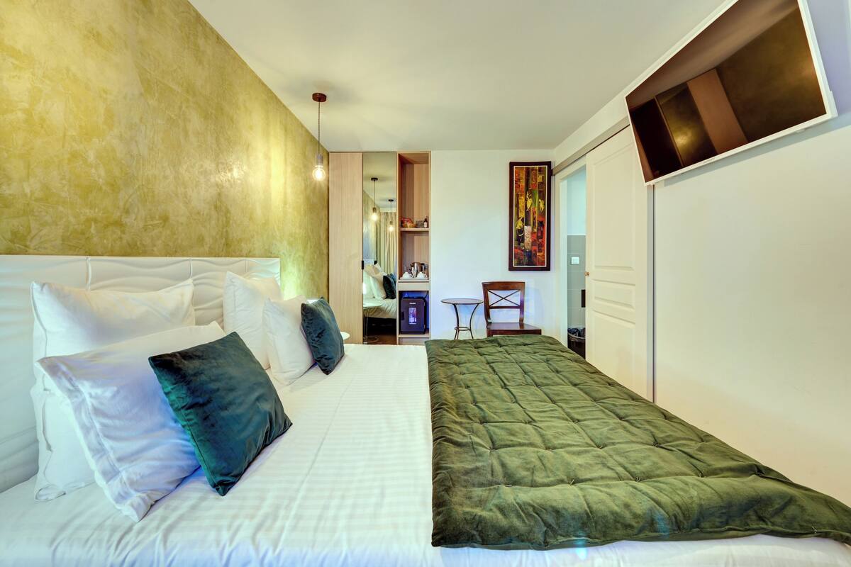 Una habitación de hotel con una cama, un edredón acolchado verde, ropa de cama blanca y un espejo grande.