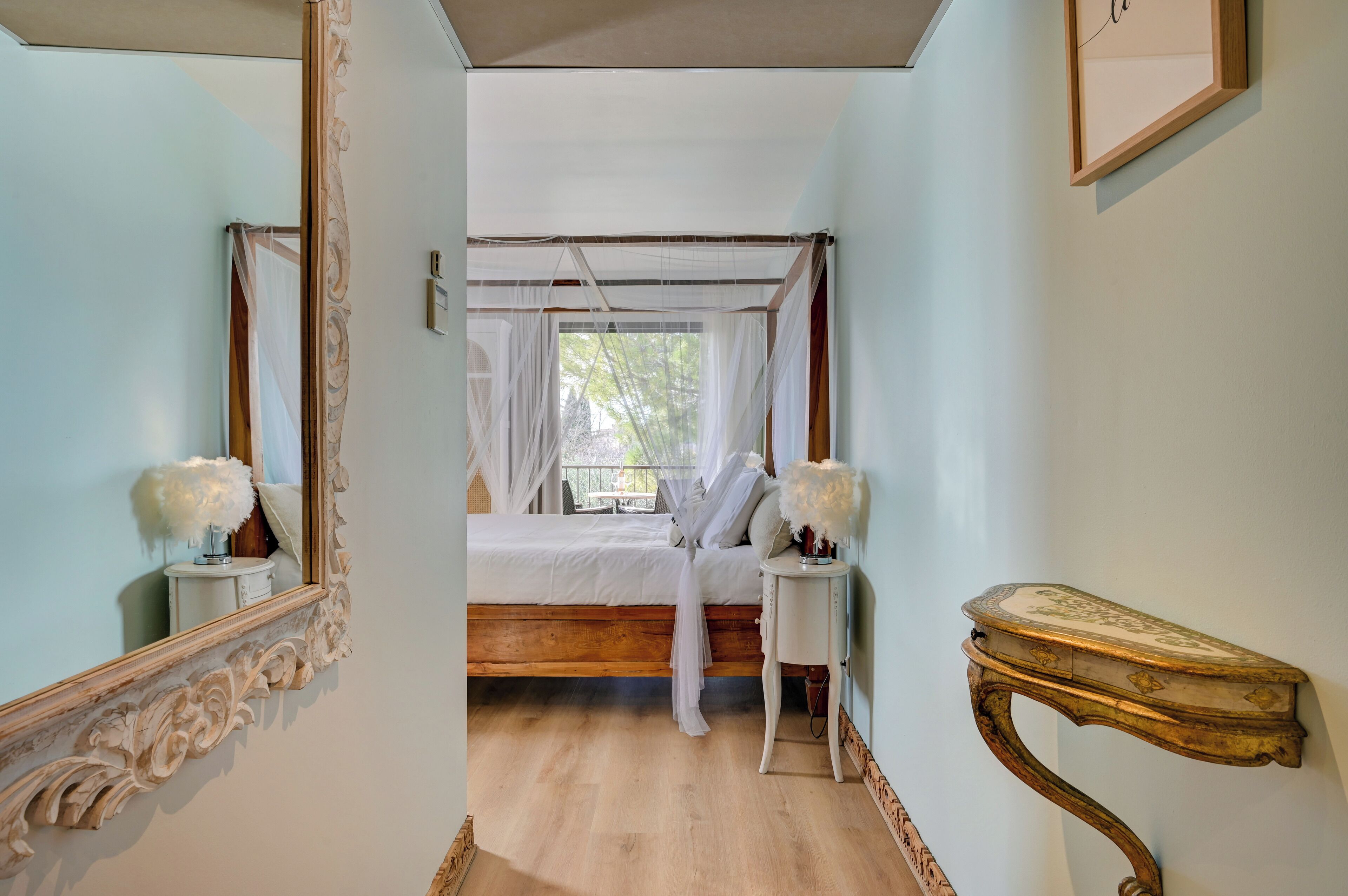 A bedroom with a canopy bed, a mirror, a bedside table, and a wall-mounted console table.