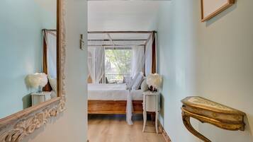 A bedroom with a canopy bed, a mirror, a bedside table, and a wall-mounted console table.