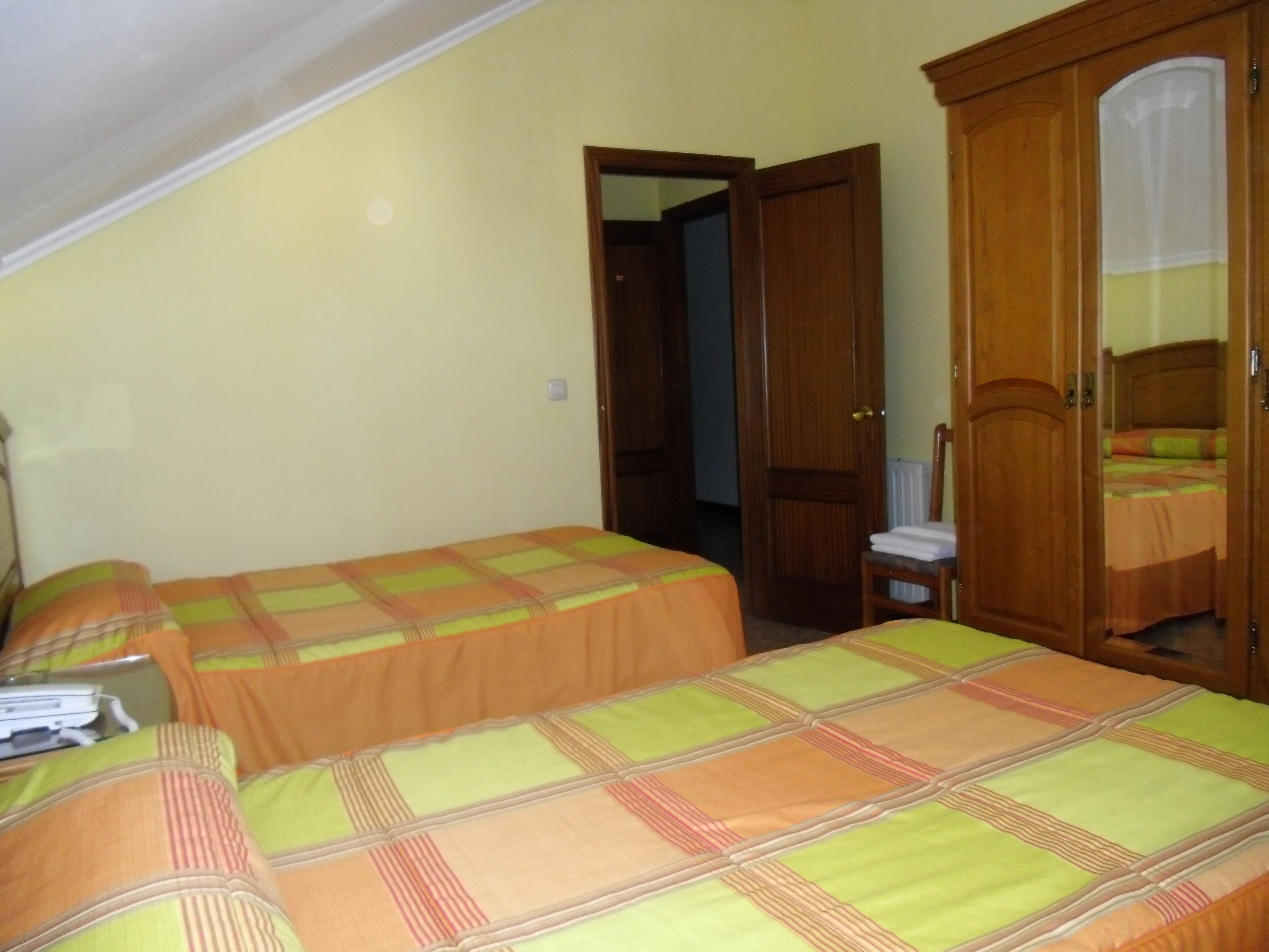 Un dormitorio con dos camas, un armario de madera y una silla pequeña.