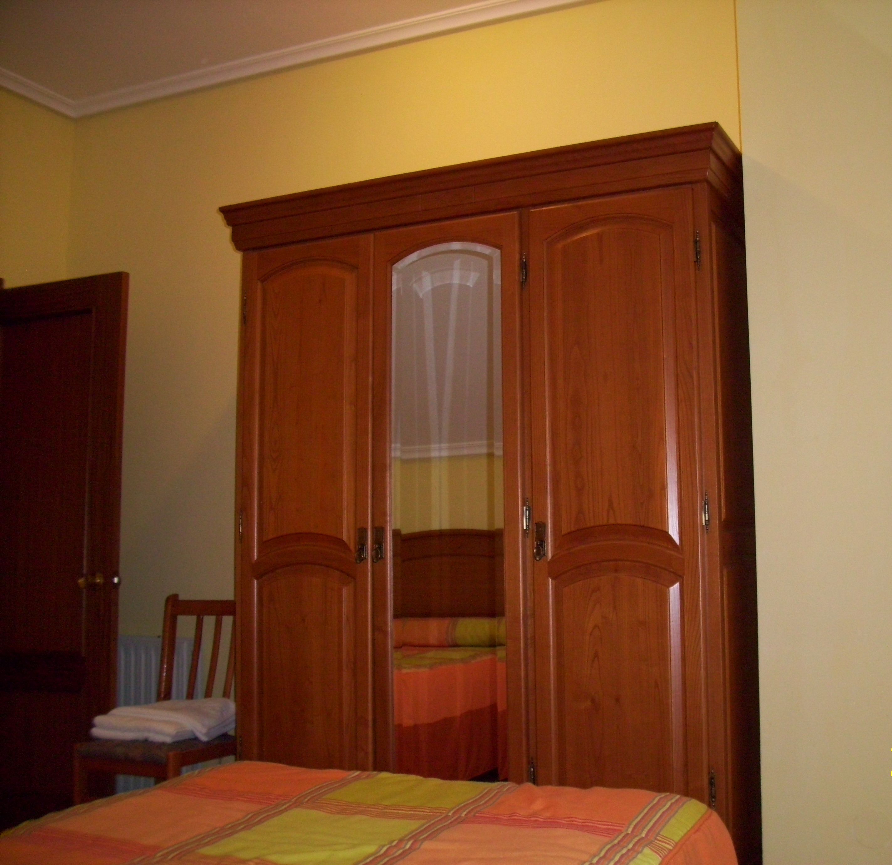 A bedroom with a wooden wardrobe, a bed with a colorful bedspread, and a chair.