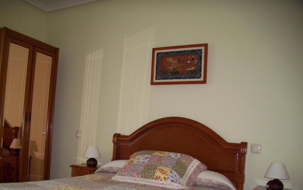 Un dormitorio con cabecera de madera, colcha acolchada, dos lámparas de noche, un cuadro enmarcado en la pared y un armario de madera.