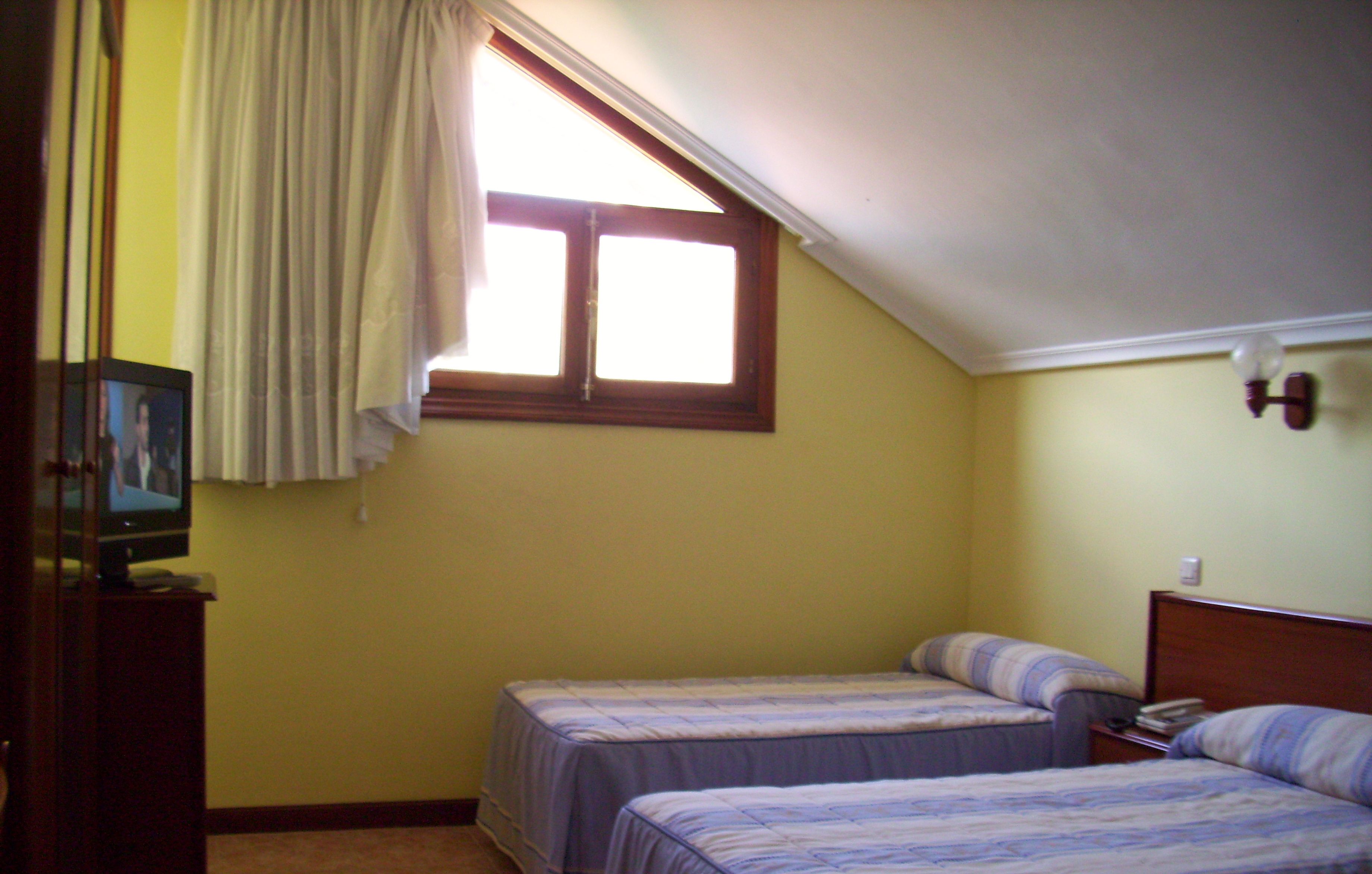 A small bedroom with two single beds, a television on a wooden stand, and a window with curtains.