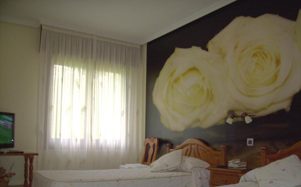 A bedroom with a bed, a nightstand, a television, and a large painting of white roses on the wall.