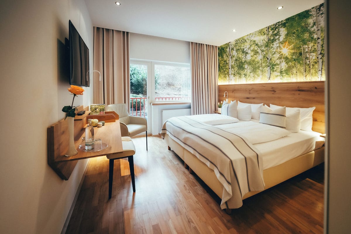 Ein modernes Hotelzimmer mit einem großen Bett, einem Schreibtisch mit Stuhl, einem an der Wand befestigten Fernseher und einem Fenster mit Vorhängen.
