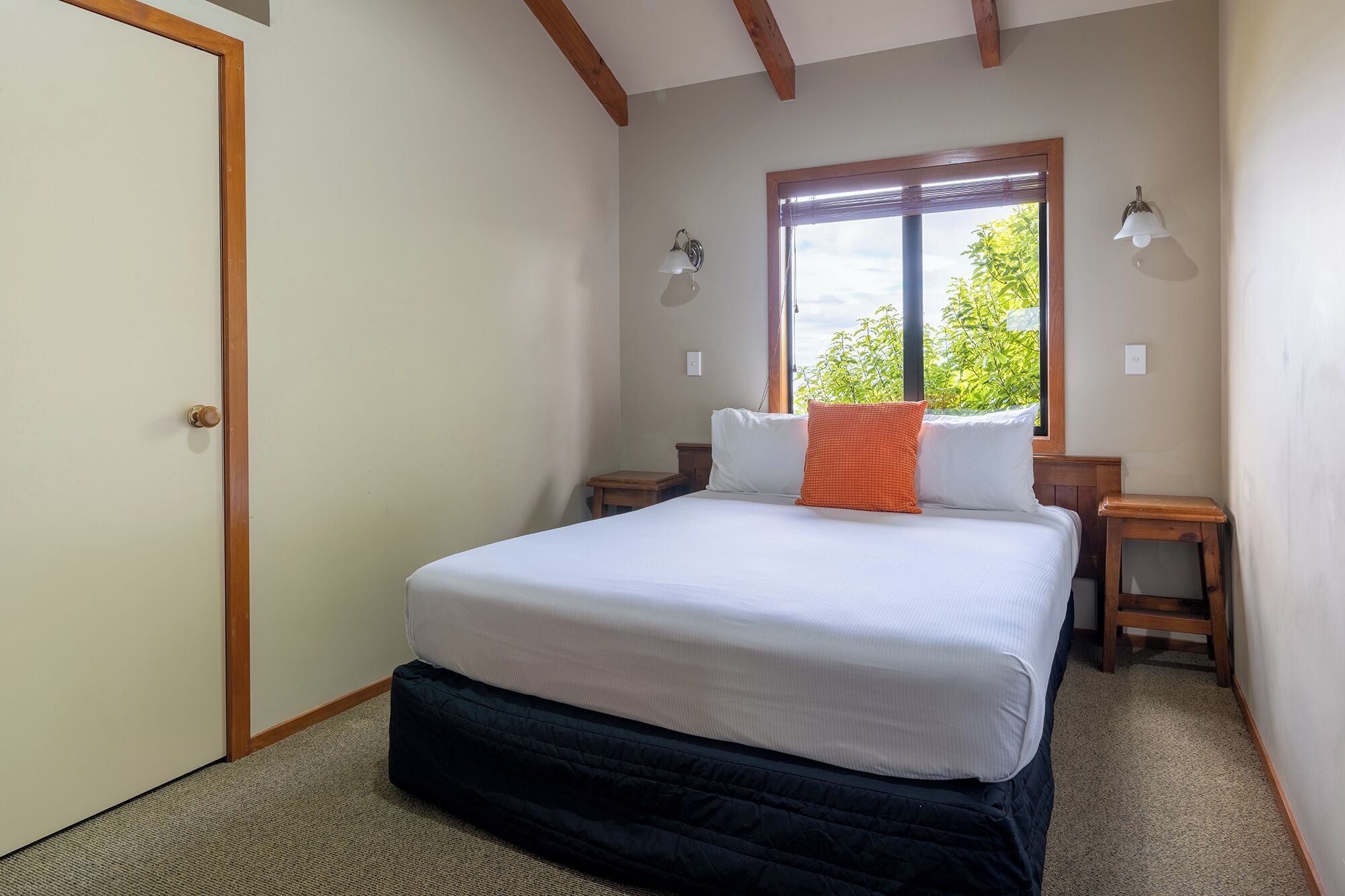 Un dormitorio con cama, dos mesitas de noche, una ventana con persianas y una puerta.