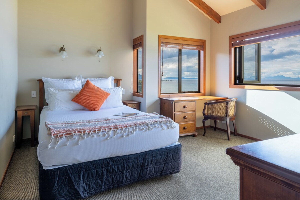 Een slaapkamer met een bed, een bureau en uitzicht op zee.