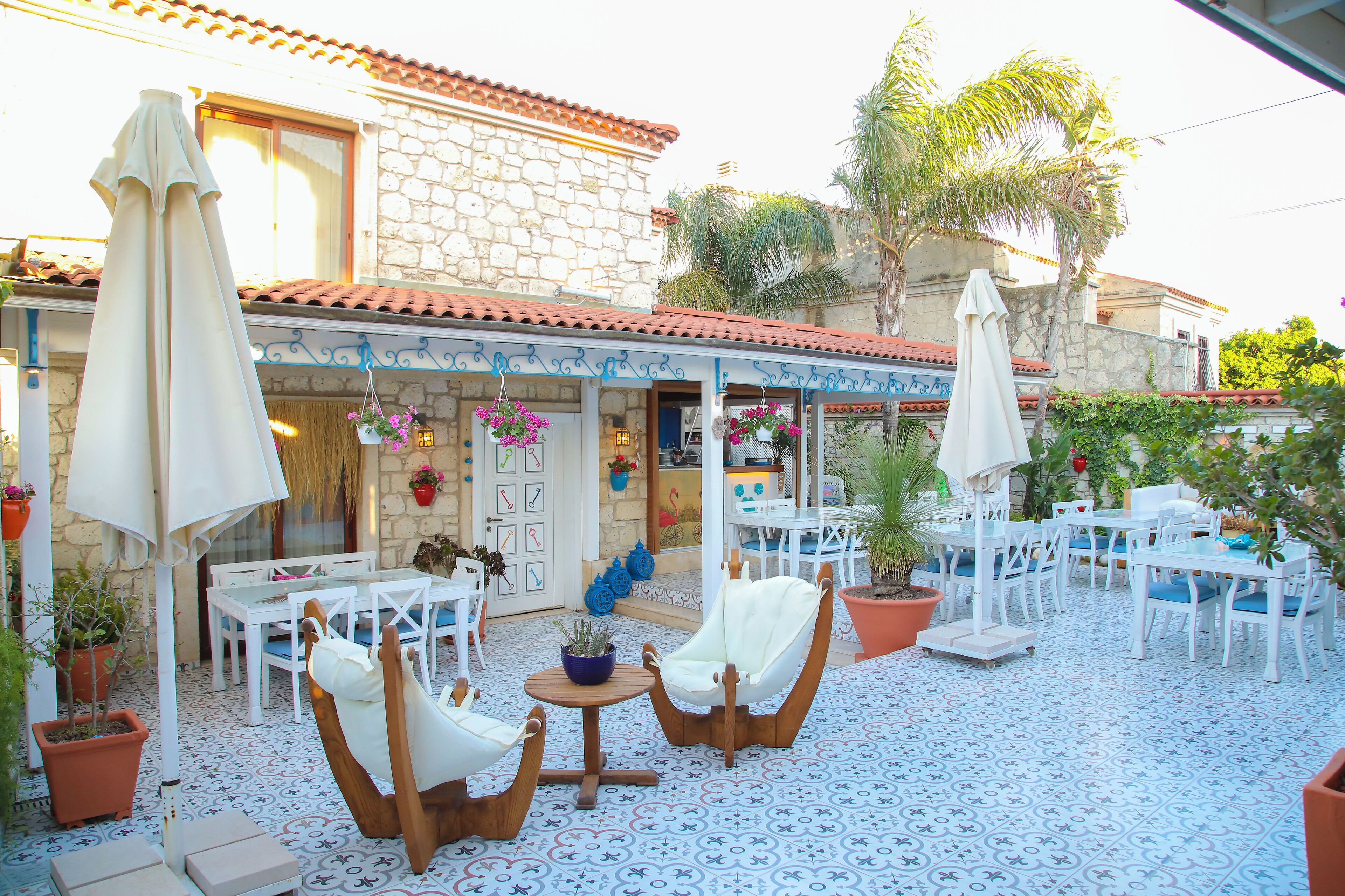 An outdoor patio with white furniture, stone walls, and potted plants.
