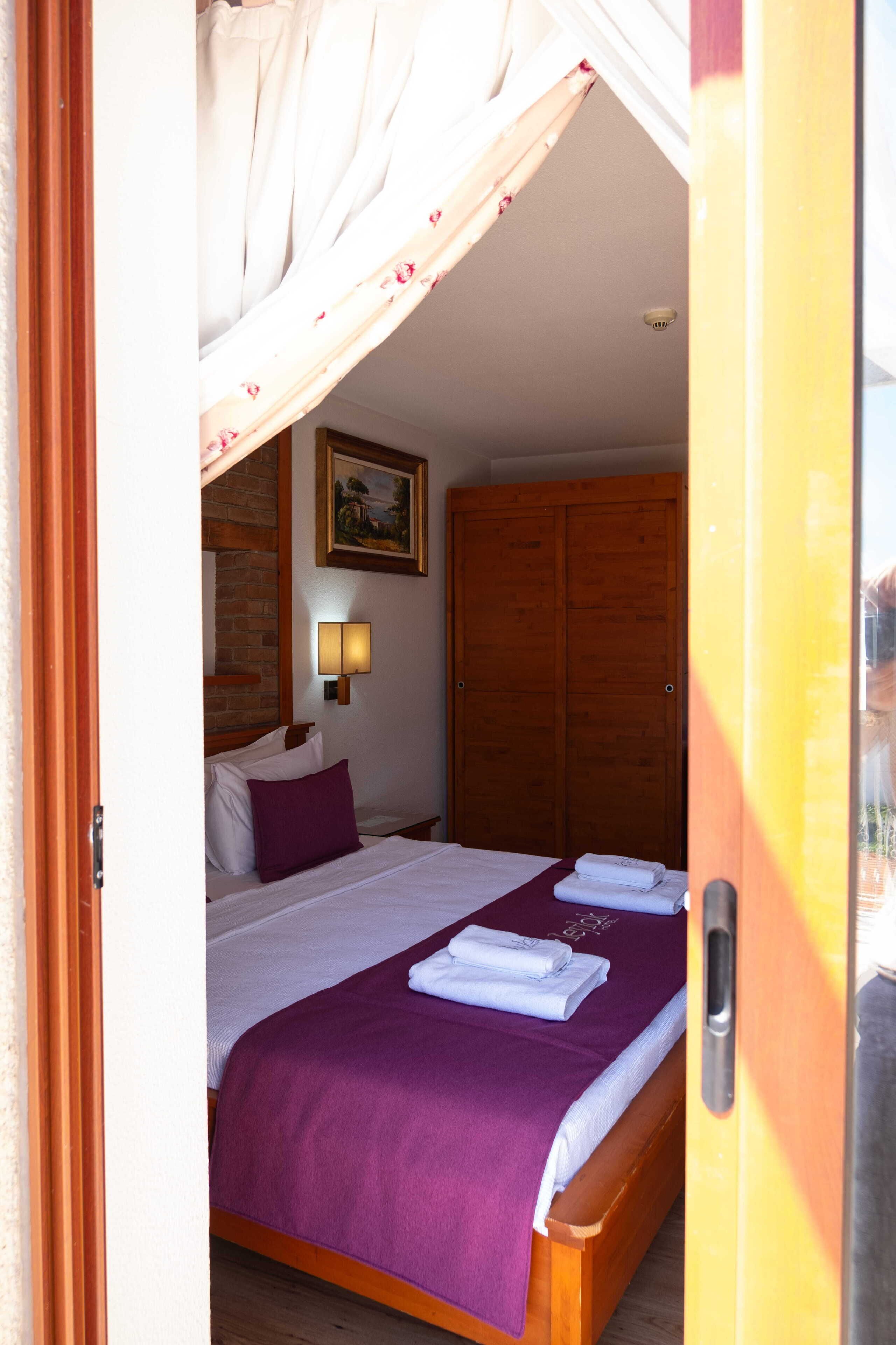A bedroom with a bed, a wooden wardrobe, a wall-mounted lamp, and a painting.