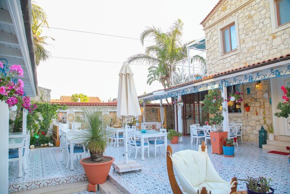 An outdoor patio with white furniture, potted plants, and a stone building with a tiled floor.