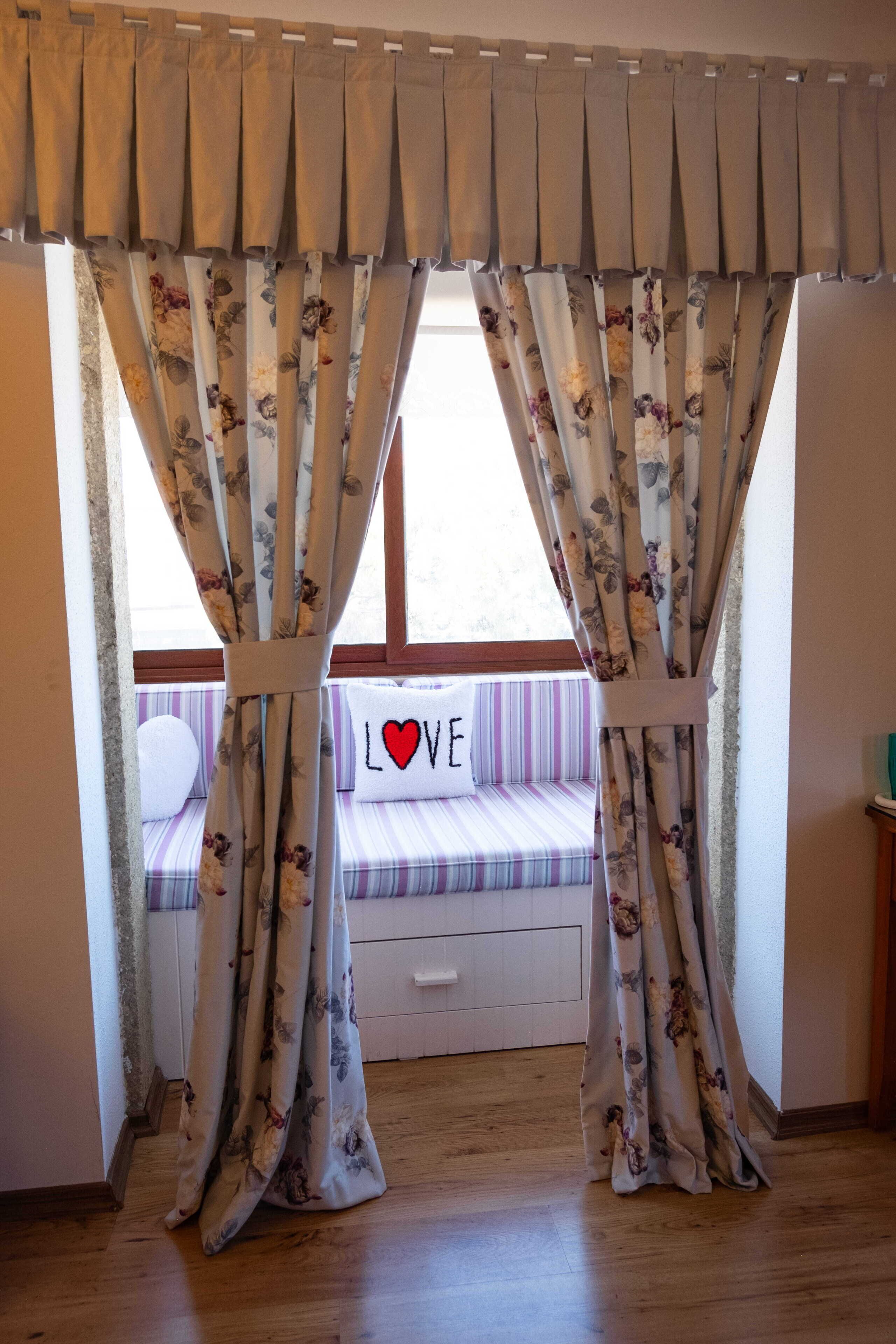 A room with a window, a bed with a striped pillow, and a sign with 'LOVE' on it.