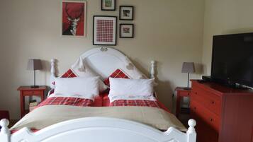 A bedroom with a white bed, red and white bedding, a television on a dresser, and framed pictures on the wall.