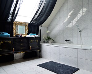 Bathroom features a black vanity, gold accents, and a large mirror with a gold frame, alongside a white bathtub and showerhead.