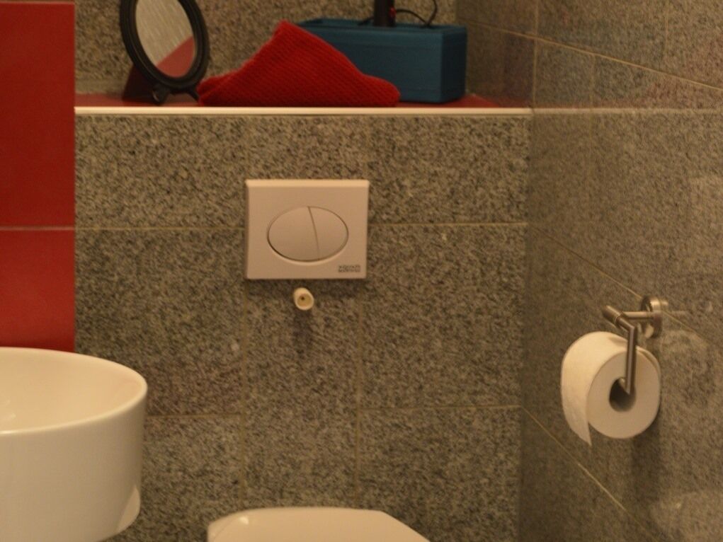 Un baño con pared de granito, un dispensador de papel higiénico y una toalla roja en un estante.