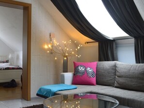 A modern living room with a glass table, a sofa with a pink owl pillow, and a blue throw pillow. - Gästehaus Gebauer (Hornbach)