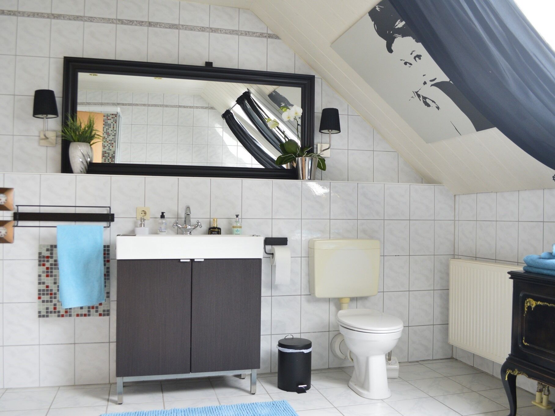 A modern bathroom with a white tiled floor, a grey cabinet, a white toilet, and a black trash bin.