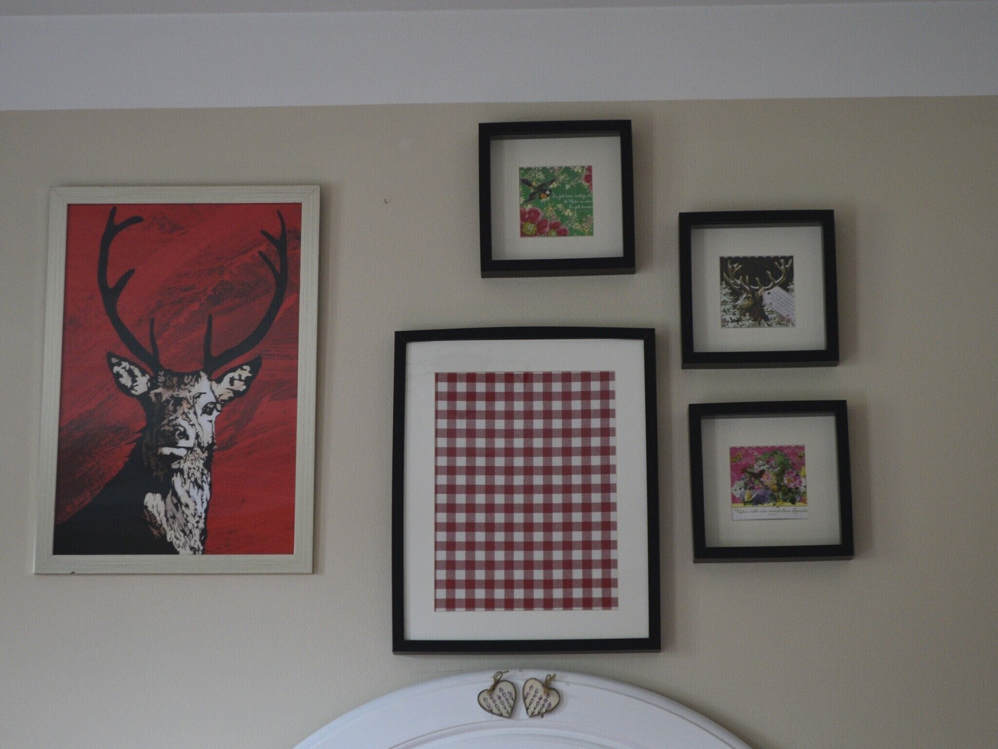 A wall with four framed pictures: a deer, a floral design, a checkered pattern, and a small floral print.
