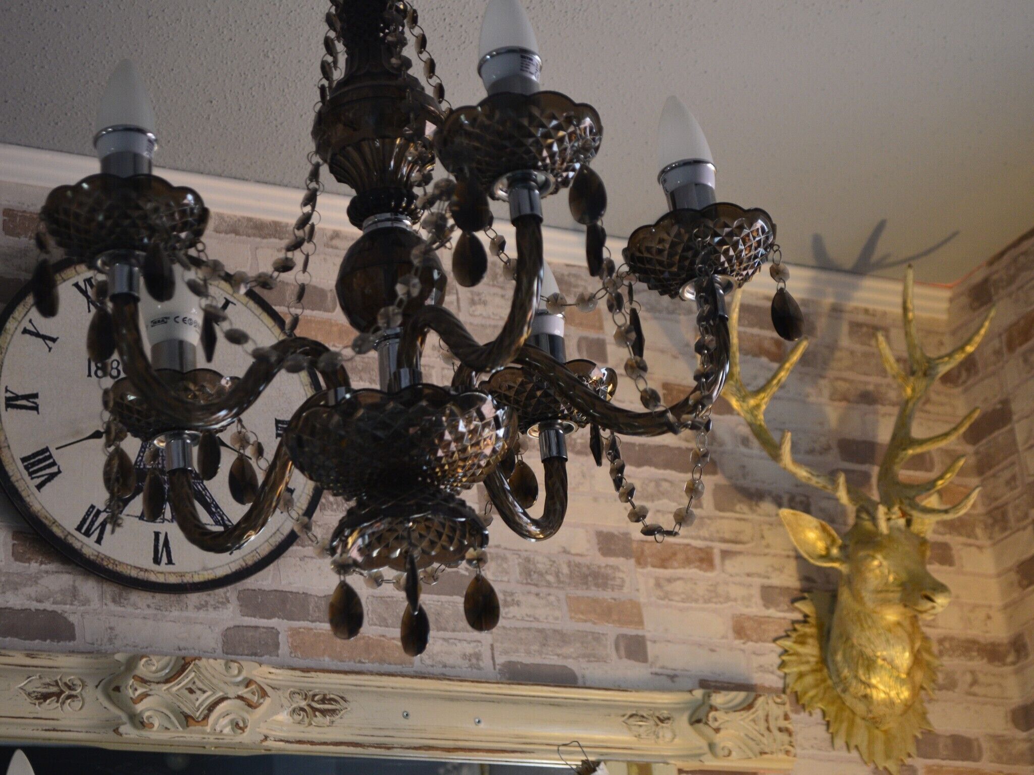 A chandelier with a clock face, a deer head decoration, and a brick wall.