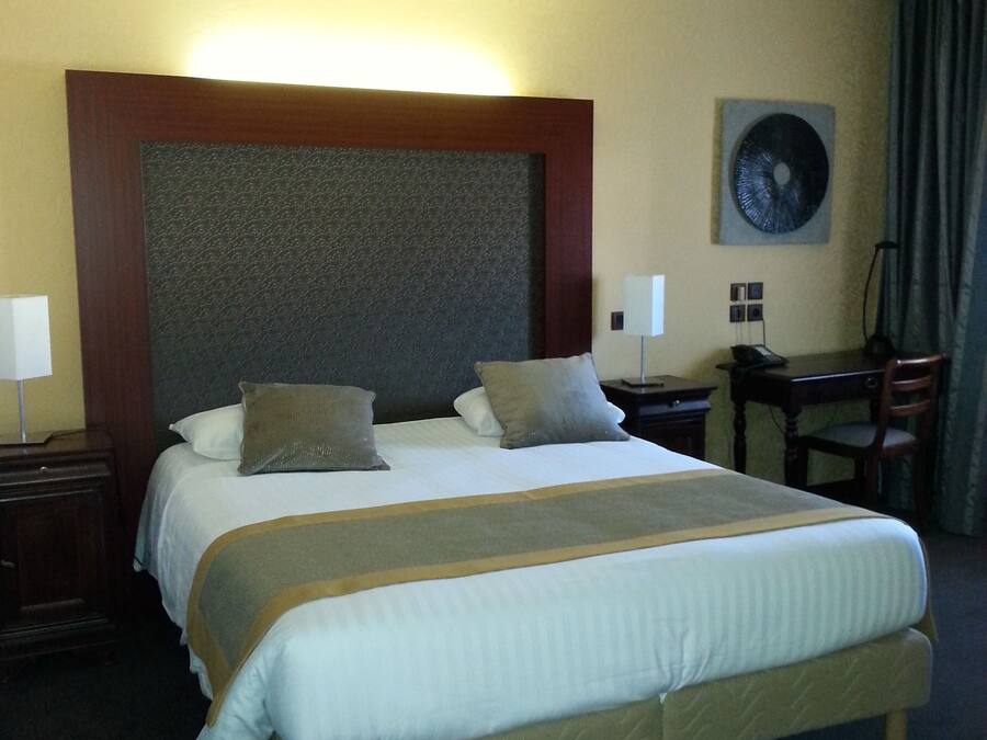 A hotel room with a large bed, a desk, a chair, a lamp, and a wall-mounted artwork.