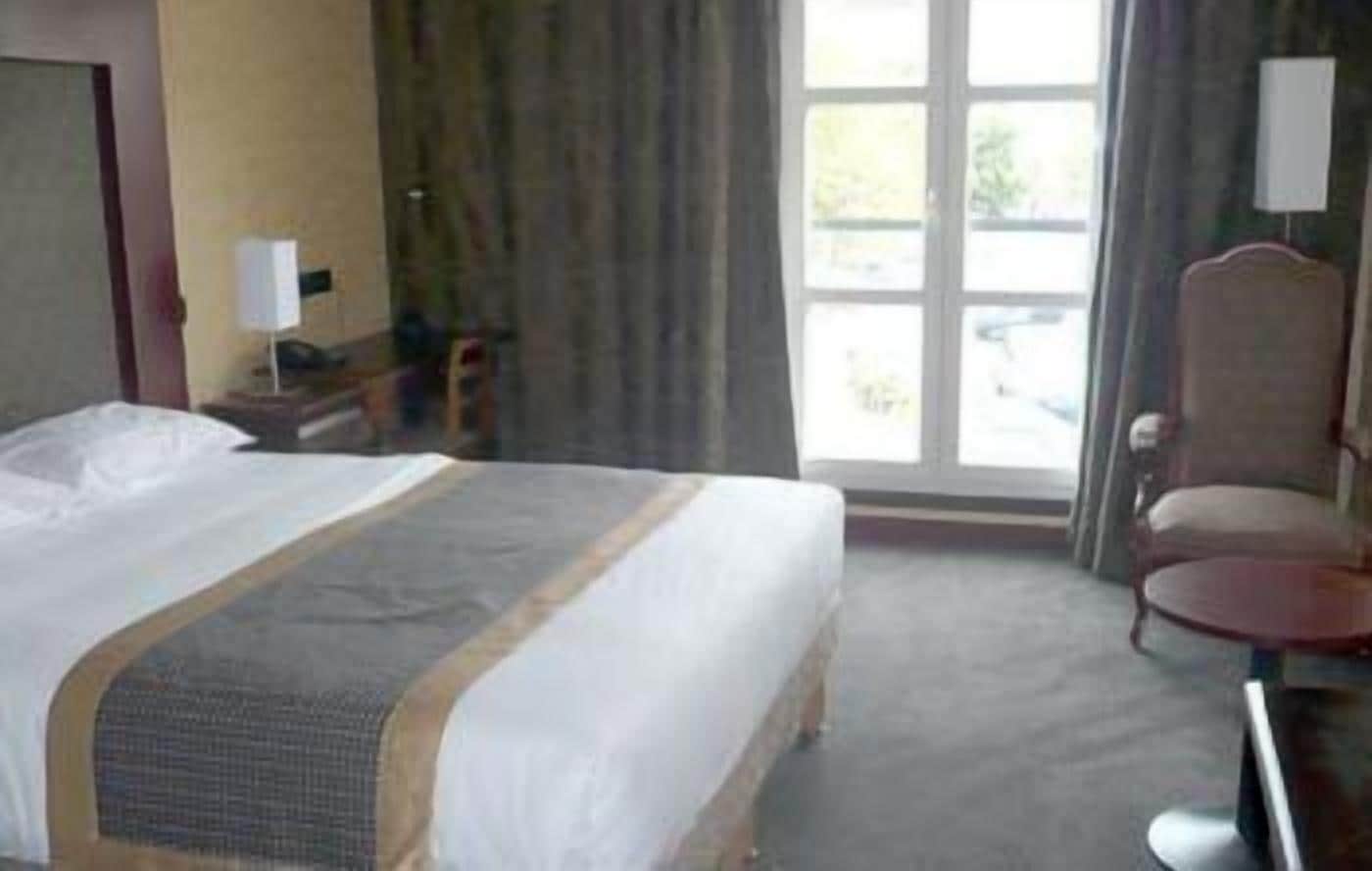 A hotel room with a large bed, a desk with a chair, a window with curtains, and a view of the outdoors.