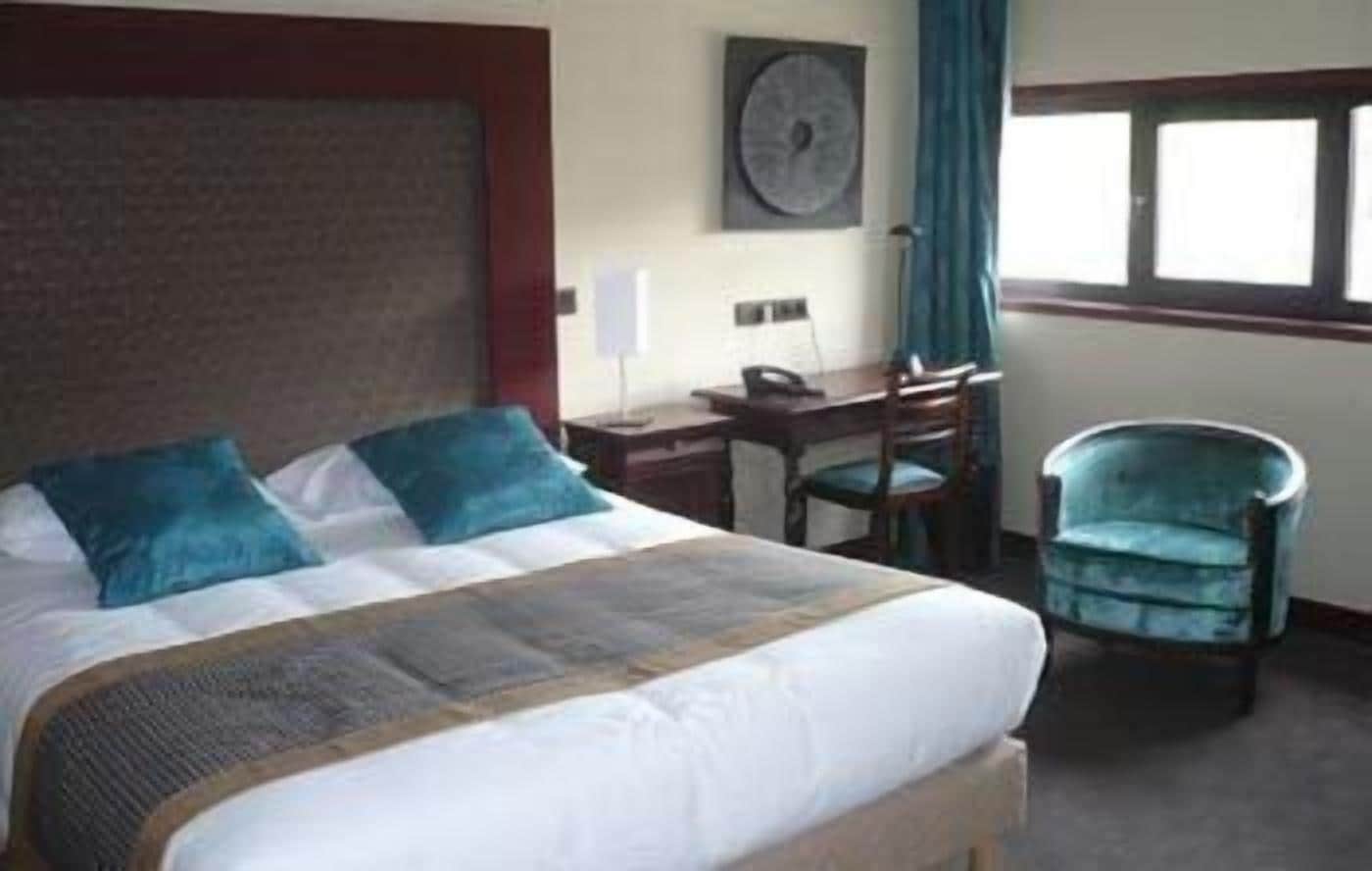 A hotel room with a bed, a desk, a chair, and a window.