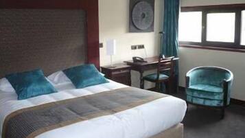 A hotel room with a bed, a desk, a chair, and a window.
