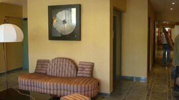 A hotel lobby with a sofa and armchair, a large clock on the wall, and a tiled floor.