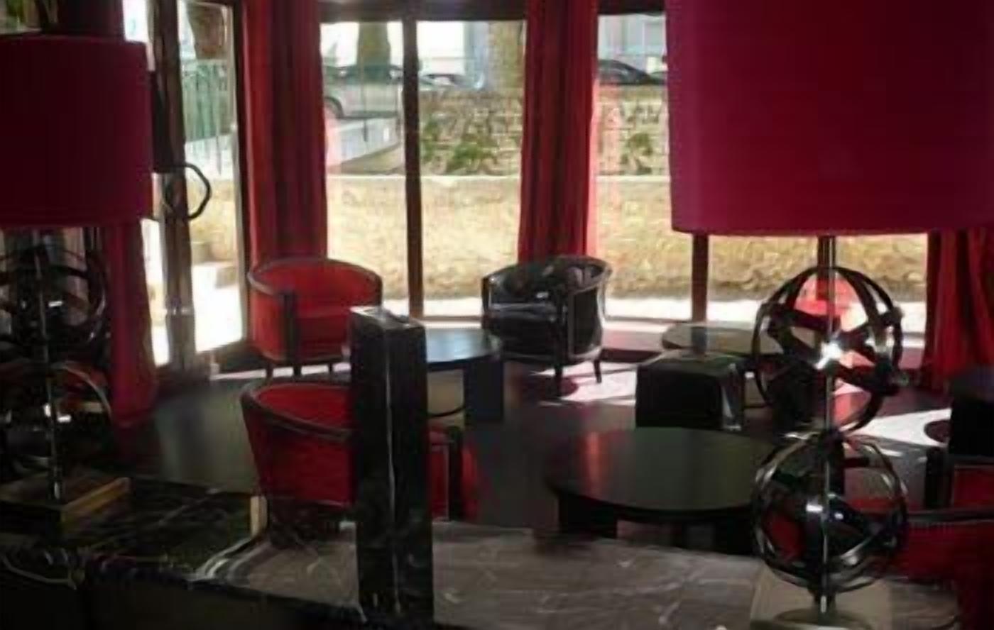 Een kamer met een ronde tafel, twee stoelen, een rood gordijn en uitzicht op het buitenland.
