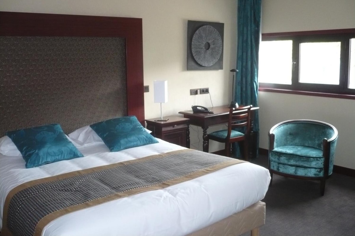 A hotel room with a large bed, a desk, a chair, and a window with curtains.
